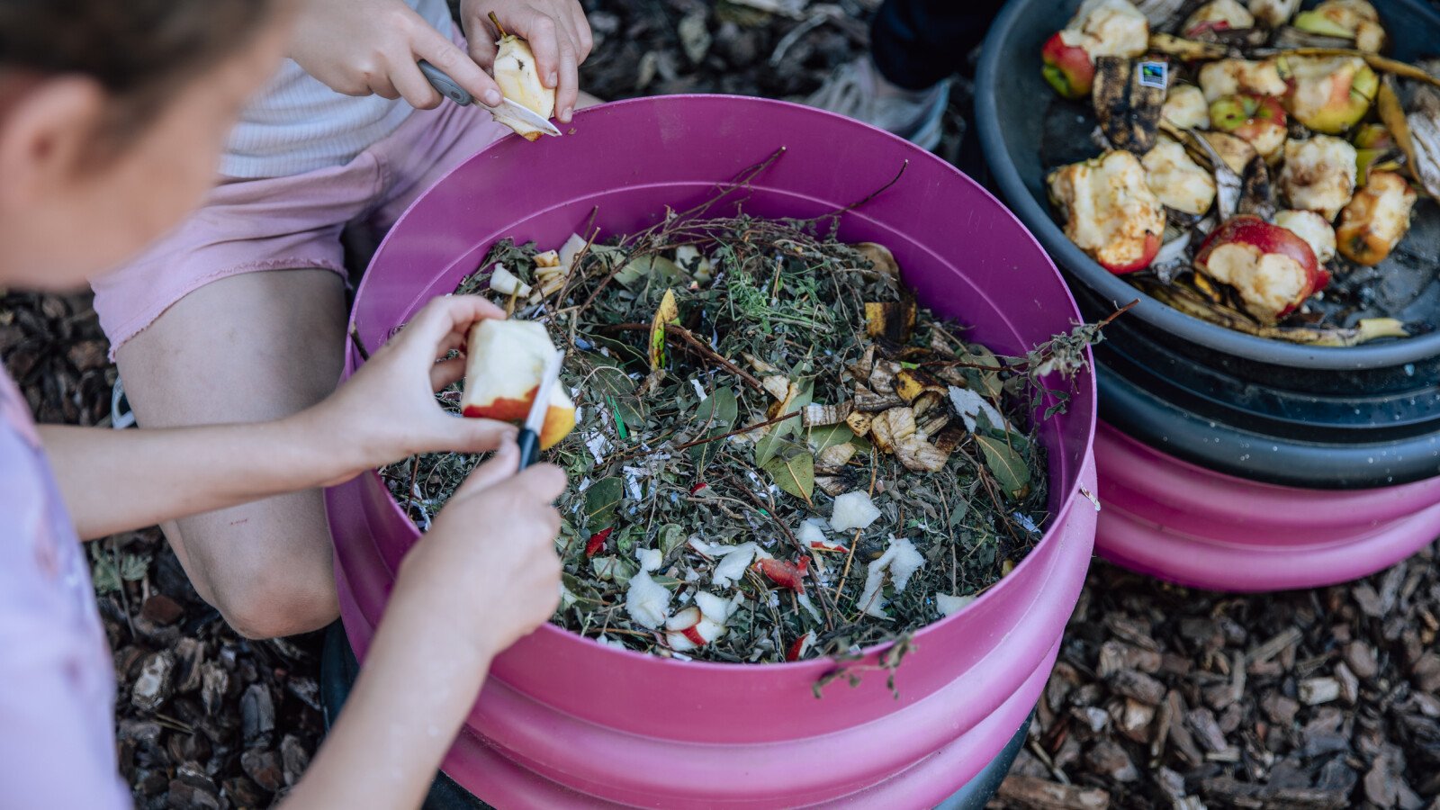 Appelschillen en ander groente-, fruit- en tuinafval worden door leerlingen toegevoegd aan een compostbak tijdens een wormenworkshop